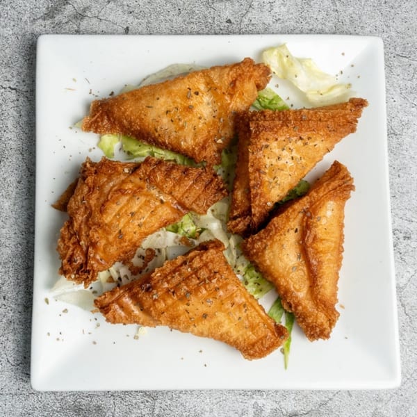 Five golden-brown, triangular Greek spanakopita pastries, garnished with herbs and lettuce on a white plate.