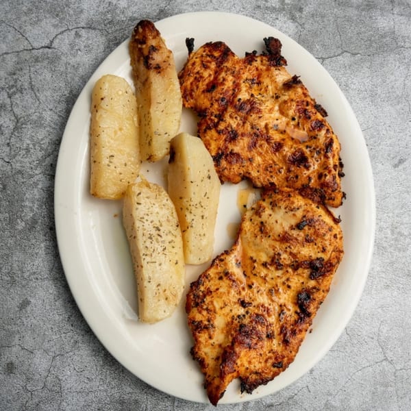 Two grilled chicken breasts and four roasted potato wedges seasoned with herbs on a white plate.