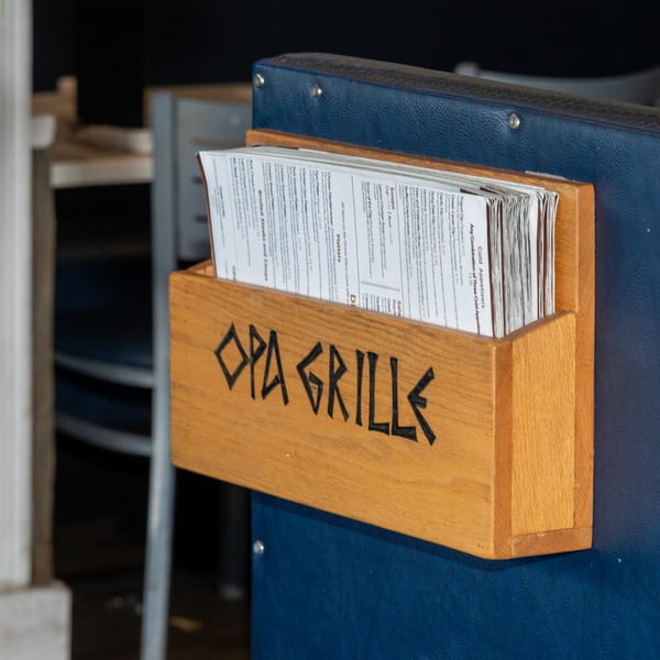 A wooden menu holder with "Opa Grille" carved into it, filled with menus on a blue surface.