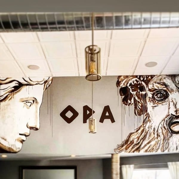 Greek-inspired mural with classical busts and "OPA" lettering on a restaurant wall.