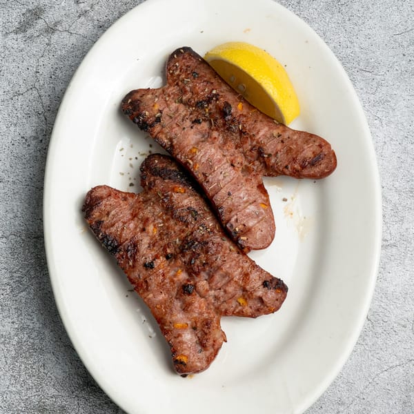 Two grilled Greek sausages (loukaniko) with a lemon wedge on a white oval plate.